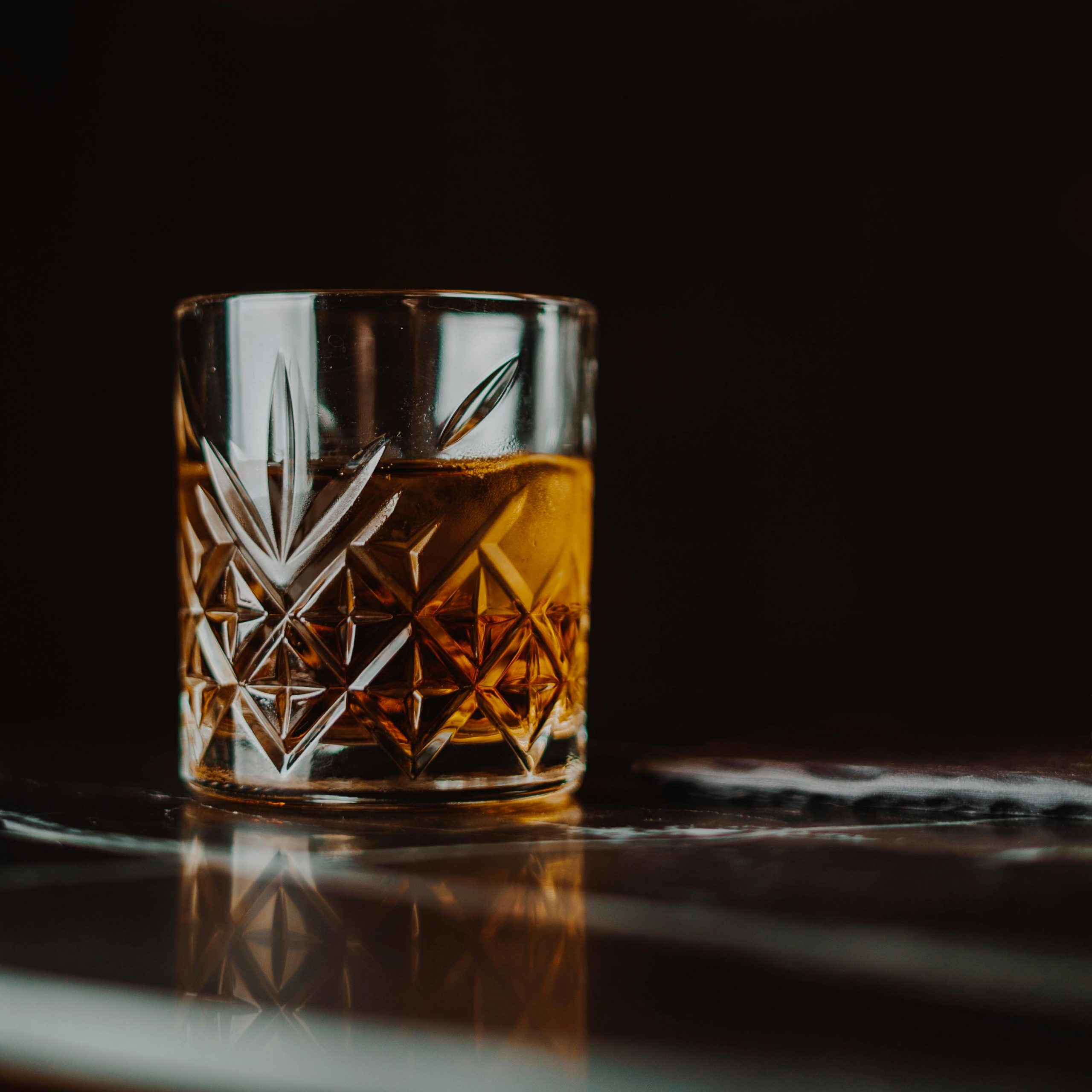 Close-up of a whiskey glass with intricate design on a reflective surface, creating a warm and inviting ambiance.