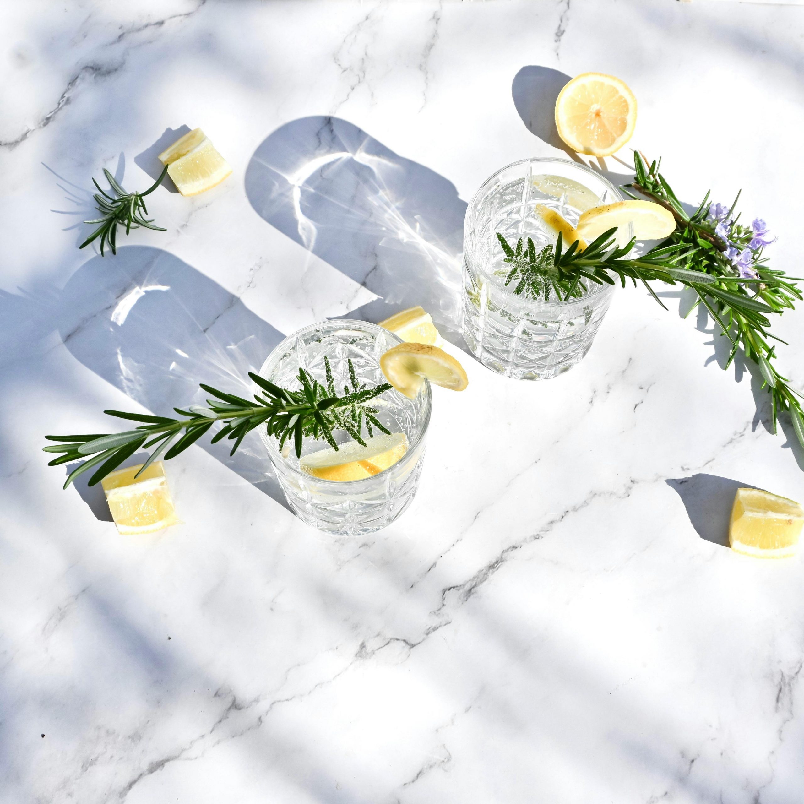 Aerial view of refreshing gin and tonic with lemon slices and rosemary on a marble surface.